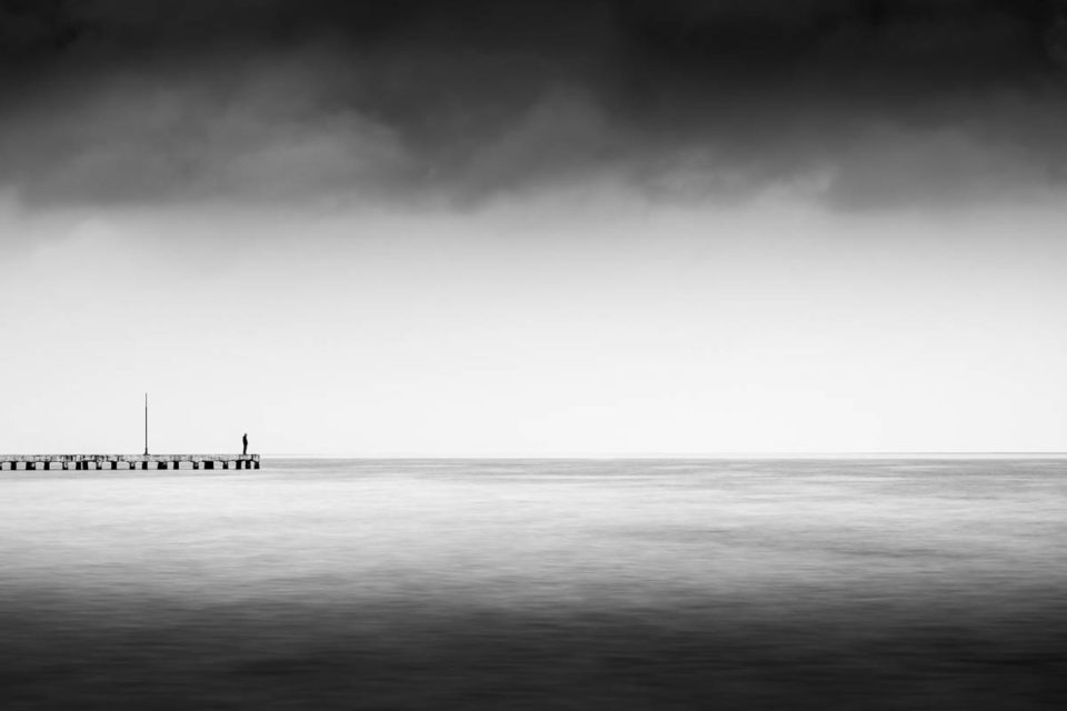 Man Standing on a Dock Staring at the Sea in Black and White